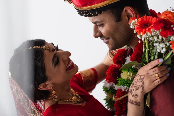 Glücklicher indischer Mann im Turban sieht zufriedene Braut mit Mehndi an, der Blumen auf weißem Grund hält — Stockfoto