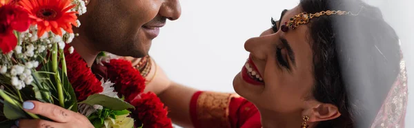 Heureuse mariée indienne avec mehndi tenant des fleurs et étreignant l'homme isolé sur blanc, bannière — Photo de stock