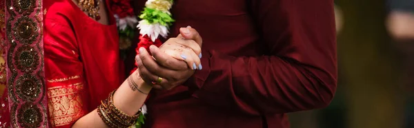 Cropped view of indian man holding hands with bride with mehndi in sari, banner — Stock Photo