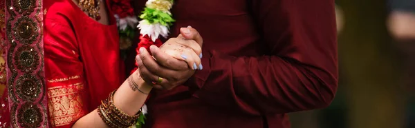 Vista recortada del hombre indio cogido de la mano con la novia con mehndi en sari, bandera - foto de stock