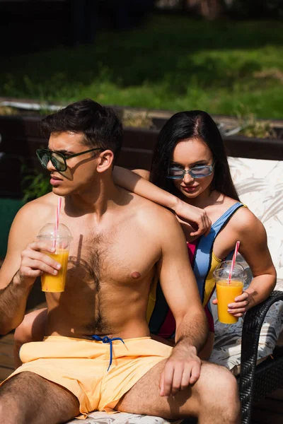 Woman with takeaway drink sitting near boyfriend on deck chair on resort — Stock Photo