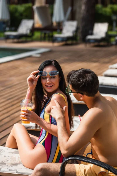 Uomo in costume da bagno seduto vicino alla ragazza con bevanda da asporto in resort — Foto stock