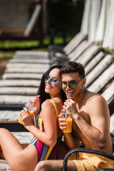 Smiling couple in swimwear drinking orange juice on deck chair — Stock Photo