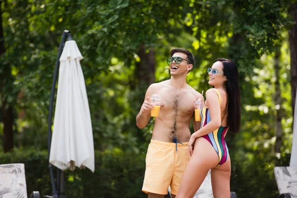 Homem alegre em calções de banho segurando bebida perto da namorada no resort — Fotografia de Stock