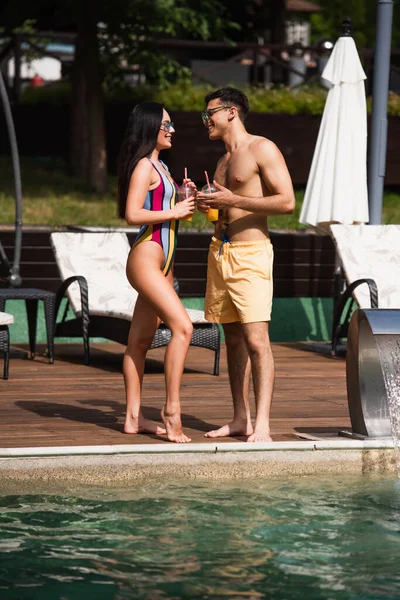Vista lateral do jovem casal com bebida tomando perto da piscina — Fotografia de Stock