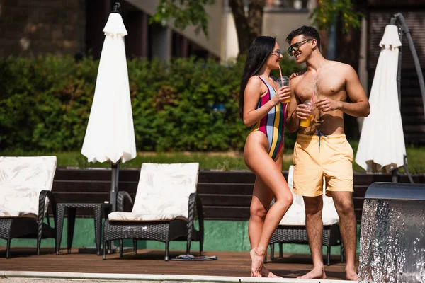 Pareja feliz con bebida para llevar de pie cerca de la fuente durante las vacaciones - foto de stock