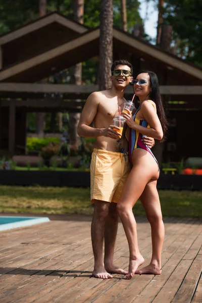 Pareja feliz en traje de baño sosteniendo copas de plástico en el resort - foto de stock