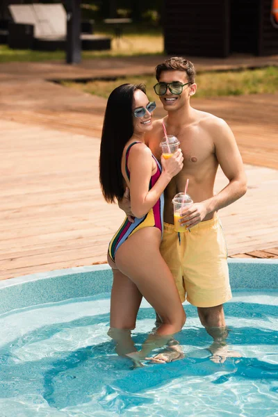 Junger Mann mit Getränk umarmt Freundin im Schwimmbad — Stockfoto