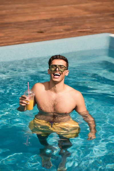 Fröhlicher Mann hält Orangensaft im Schwimmbad — Stockfoto