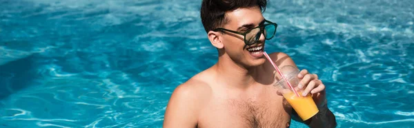 Uomo sorridente in occhiali da sole che beve succo d'arancia in piscina, banner — Foto stock