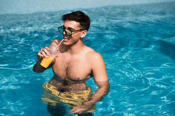 Jovem relaxante com suco de laranja na piscina — Fotografia de Stock