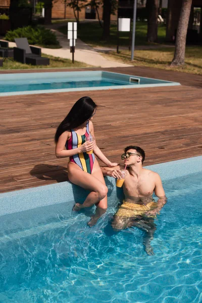 Casal jovem com suco de laranja descansando na piscina — Fotografia de Stock