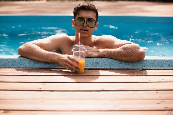 Mann mit Sonnenbrille hält Plastikbecher mit Orangensaft im Schwimmbad — Stockfoto