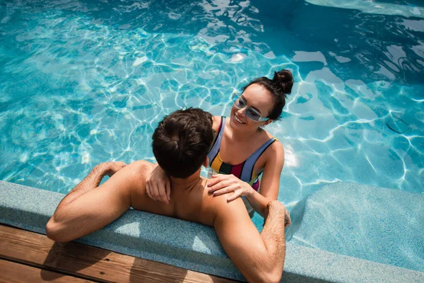 Vue aérienne d'une femme positive embrassant un homme torse nu dans une piscine — Photo de stock