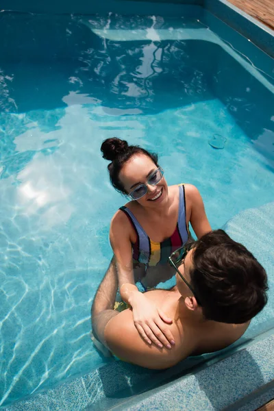 Visão aérea da mulher sorridente descansando com namorado em óculos de sol na piscina — Fotografia de Stock