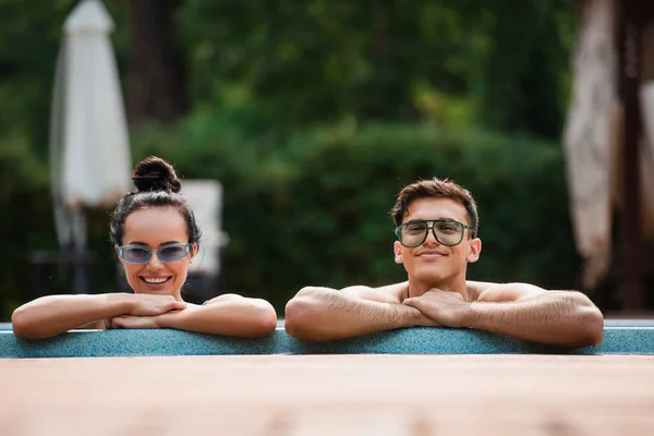 Smiling couple looking at camera near poolside on resort — Stock Photo