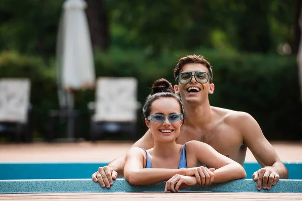 Hombre sin camisa de pie cerca de novia en la piscina durante las vacaciones - foto de stock