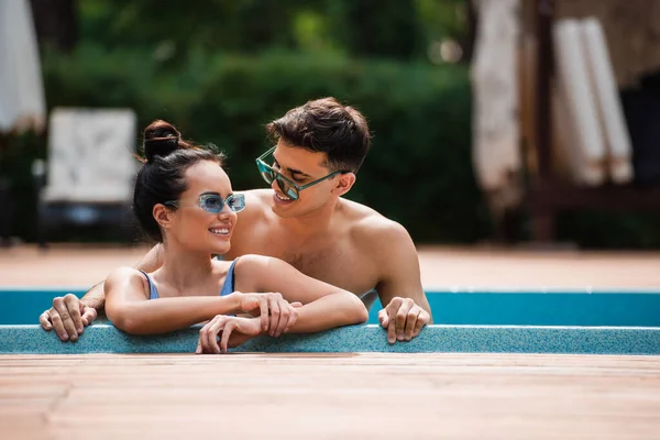 Hombre sonriente mirando a su novia en la piscina en el complejo - foto de stock