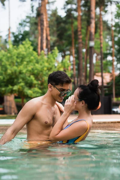 Hombre sonriente mirando a su novia sosteniendo gafas de sol en la piscina — Stock Photo