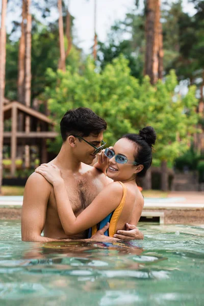 Joven abrazando novia sonriente mirando a la cámara en la piscina - foto de stock