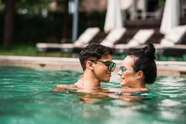 Vue latérale du couple souriant en lunettes de soleil relaxant dans la piscine — Photo de stock