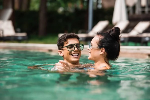 Femme souriante relaxant avec jeune petit ami dans la piscine — Photo de stock