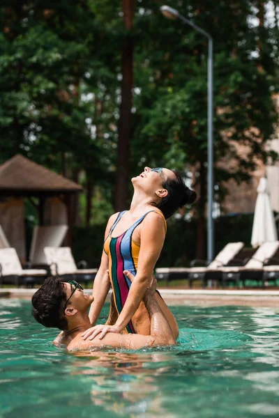 Vue latérale de l'homme souriant levant petite amie au-dessus de la piscine — Photo de stock