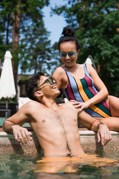 Mujer sonriente en gafas de sol mirando al novio en la piscina - foto de stock