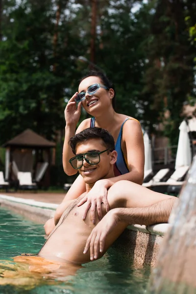 Bella donna in occhiali da sole abbracciare fidanzato bagnato in piscina — Foto stock