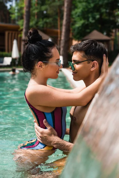 Vista lateral do jovem casal abraçando uns aos outros na piscina — Fotografia de Stock