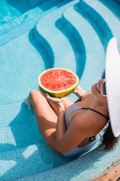 Vista aérea de una mujer sonriente con gafas de sol sosteniendo sandía en la piscina - foto de stock