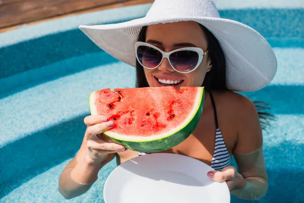 Donna felice che tiene pezzo di anguria e piatto in piscina durante il fine settimana — Foto stock