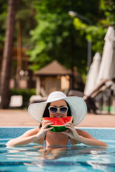 Mujer joven en la piscina comiendo sandía durante las vacaciones - foto de stock