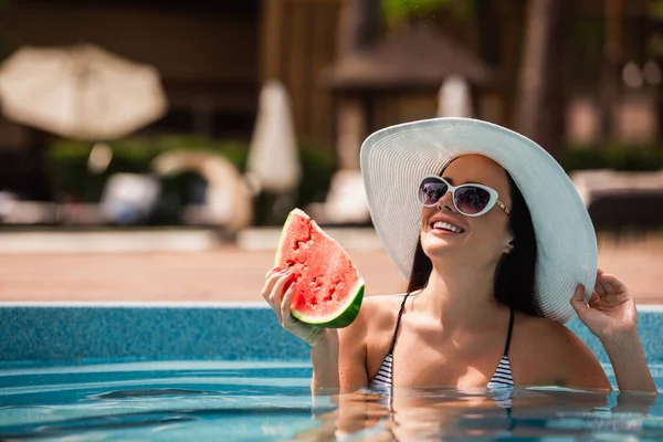 Cheerful woman holding watermelon in swimming pool on resort — Stock Photo