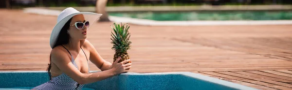 Brune femme au chapeau de soleil tenant l'ananas dans la piscine en station balnéaire, bannière — Photo de stock