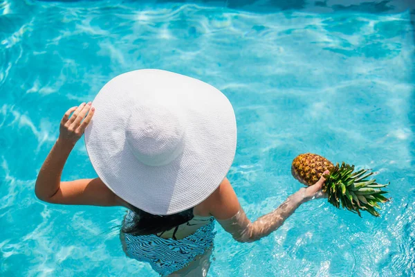 Overhead view of woman in sun hat holding pineapple in swimming pool — Stock Photo