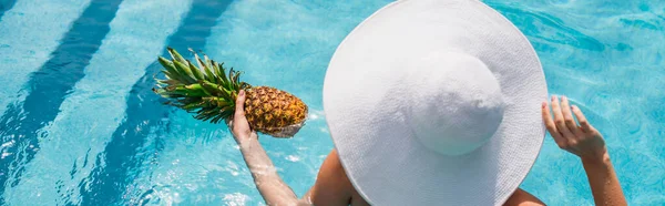 Vista aerea della donna in cappello da sole bianco con ananas in piscina, banner — Foto stock