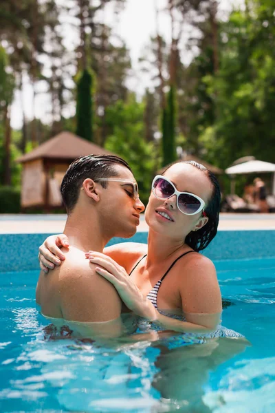 Hombre besando bonita novia en gafas de sol en la piscina - foto de stock