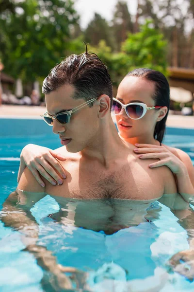 Junge Frau mit Sonnenbrille vor verschwommenem Hintergrund umarmt Freund im Pool — Stockfoto
