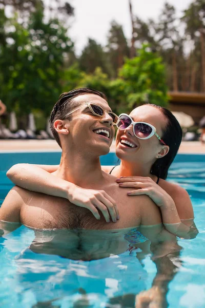 Lächelnde Frau mit Sonnenbrille umarmt fröhlichen Freund im Schwimmbad — Stockfoto