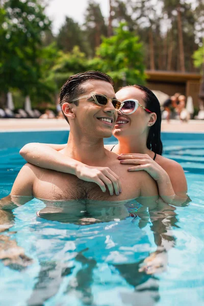 Sonriente pareja abrazándose en la piscina en el complejo - foto de stock