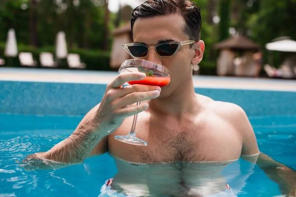 Man in sunglasses drinking cocktail in swimming pool — Stock Photo