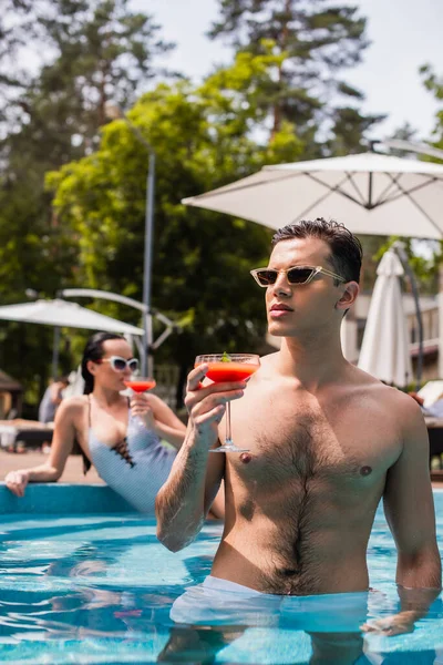 Young man holding alcoholic cocktail in swimming pool — Stock Photo