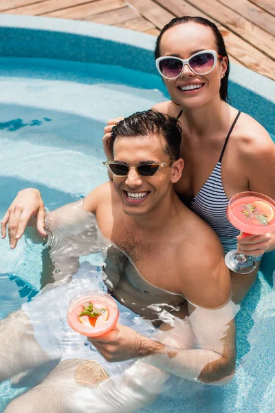 Blick aus der Vogelperspektive auf ein fröhliches Paar, das Cocktails im Schwimmbad hält — Stockfoto