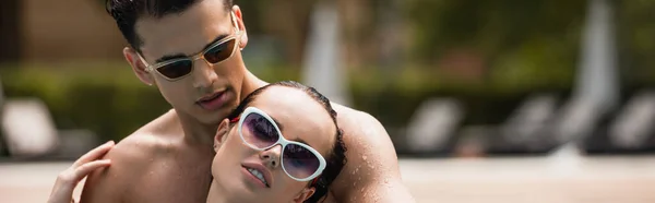 Hombre sin camisa en gafas de sol abrazando novia durante el fin de semana, pancarta - foto de stock