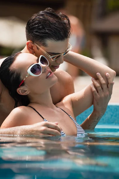 Surface level of man touching hand of sexy girlfriend in swimming pool — Stock Photo