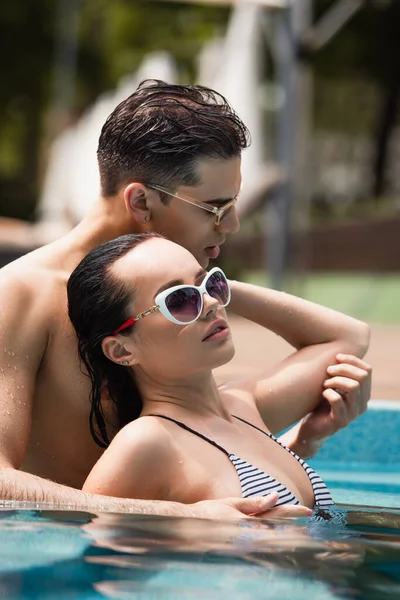 Surface level of sexy couple in sunglasses relaxing in swimming pool — Stock Photo