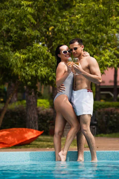 Mulher sorridente abraçando namorado com copo de vinho perto da piscina — Fotografia de Stock