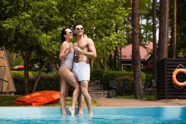 Pareja feliz sosteniendo copas de vino cerca de la piscina durante las vacaciones - foto de stock