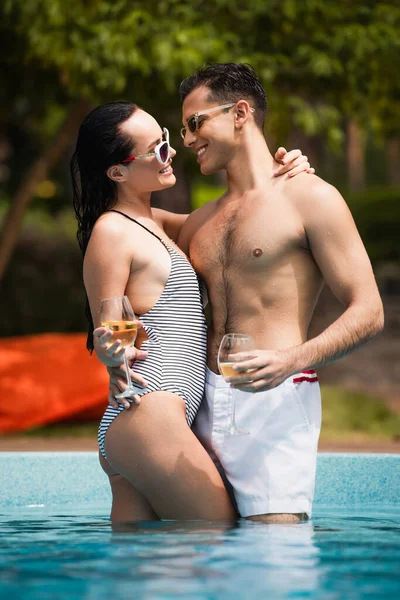 Vue latérale de la femme souriante avec petit ami câlin vin dans la piscine — Photo de stock